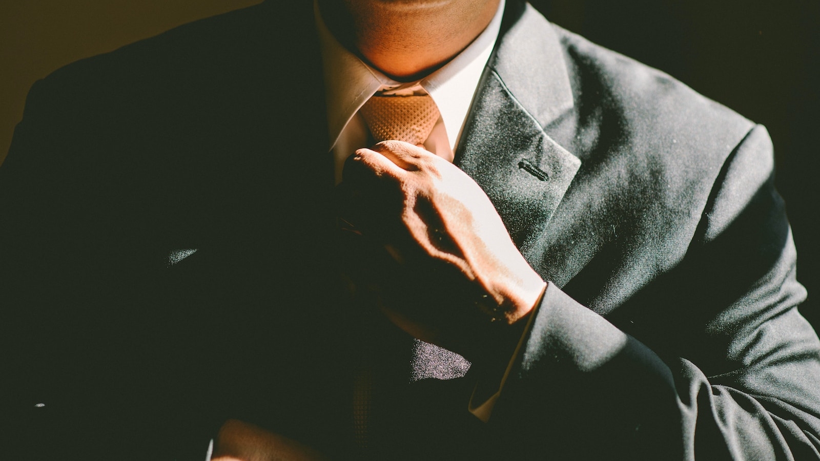 A man in a black suit loosening his tie